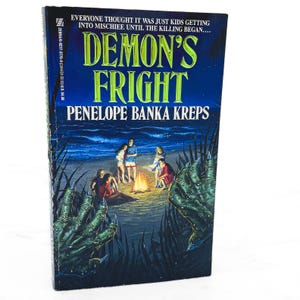 May include: A paperback book titled "Demon's Fright" by Penelope Banka Kreps. The cover features a dark blue night scene with a bonfire on a beach and figures gathered around it. The title is in large, yellow letters.