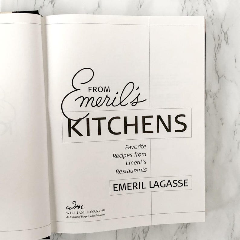 以下が含まれることがあります： 「From Emeril's Kitchens」というタイトルがエレガントな筆記体と太字のブロック文字で書かれた、開かれた料理本のページ。その下に、エメリル・ラガッセ著「Favorite Recipes from Emeril's Restaurants」と書かれています。ウィリアム・モローのインプリントが見えます。