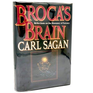 May include: A hardcover book titled "Broca's Brain" by Carl Sagan. The book has a black cover with red and gold lettering. The cover also features a gold illustration of a human face.