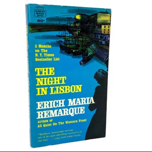 May include: A vintage paperback book titled The Night in Lisbon by Erich Maria Remarque. The cover features a bright blue background with yellow text, a black silhouette of a person, and an illustration of a harbor scene at the top.