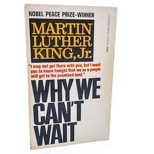 May include: Vintage paperback book titled "Why We Can't Wait" by Martin Luther King, Jr. The cover features bold black and yellow text with a quote in red. The book is a Signet Book.