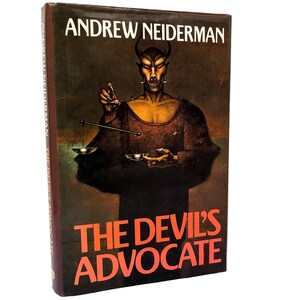 May include: A hardcover book titled The Devil's Advocate by Andrew Neiderman. The cover features a dark, textured illustration of a horned, demonic figure holding a set of scales. The title is printed in large, bold orange letters at the bottom.