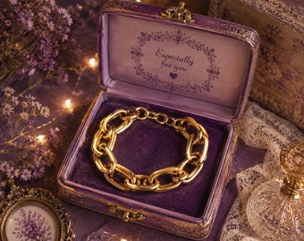 Puede incluir: Una pulsera de eslabones gruesos en tono dorado dentro de un joyero rectangular forrado de terciopelo morado. La tapa interior de la caja presenta un borde floral decorativo y el texto impreso "Especially for you" con un pequeño icono de corazón.