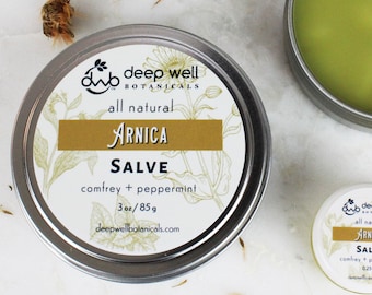 May include: A silver tin of Deep Well Botanicals Arnica Salve with a white label that reads "all natural Arnica Salve comfrey + peppermint 3oz/85g deepwellbotanicals.com".