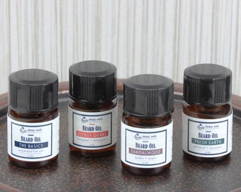 May include: Four small brown glass bottles with black lids and white labels. Each bottle contains beard oil with different scents: The Basics, Citrus Quake, Sandalwood, and Fresh Earth.