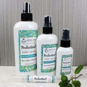 May include: Four bottles of toilet spray in various sizes. The bottles are white with green and white labels. The labels say "PooFection! toilet spray Eucalyptus Mint Mist, Make & Marvel" and list the size in ounces. The largest bottle is 8 fl oz, the next is 4 fl oz, and the smallest is 2 fl oz. There is a small, clear travel-sized bottle of toilet spray in the foreground. The bottles are on a white surface with a sprig of green mint leaves.