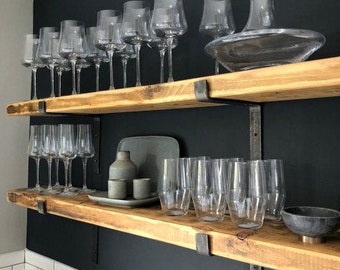 Puede incluir: Dos estantes de madera con soportes de metal negro, que sostienen una colección de copas de vino de vidrio transparente y una decantador. Los estantes están montados en una pared negra.