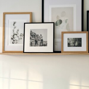 May include: Four framed pictures on a shelf. The pictures are in black and white and feature a variety of subjects, including a plant, a family, and abstract shapes.