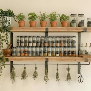 May include: A rustic wooden spice rack with two shelves, holding glass jars of spices, potted herbs, and hanging dried herbs. The rack is mounted on a light-colored wall, creating an organized and functional kitchen storage solution.