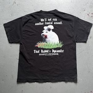 Op de afbeelding: Zwart T-shirt met een afbeelding van een wit konijn met rode tanden en de tekst "We'll not risk another frontal assault. That Rabbit's Dynamite!" en "MONTY PYTHON" in witte gotische letters.