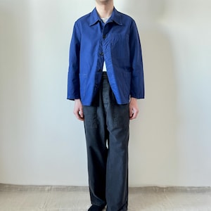 May include: A blue jacket with three buttons and two front pockets. The jacket is paired with dark gray pants. The outfit is casual and suitable for everyday wear. The jacket's color is a vibrant blue.