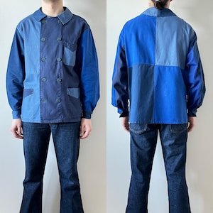 May include: A patchwork blue jacket with a double-breasted design, featuring various shades of blue. The jacket has two front pockets and a collared neckline. The model is also wearing dark blue jeans.