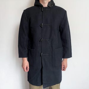 May include: A black duffel coat with a hood and toggle closures. The coat has two large front pockets and is knee-length. The coat is made of a heavy fabric, suitable for cold weather. The coat's length is approximately 40 inches.