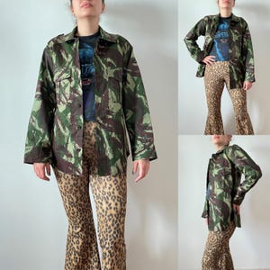 Peut inclure: Veste à imprimé camouflage vert, marron et beige, avec deux poches poitrine et une fermeture boutonnée. Elle est associée à un pantalon évasé à imprimé léopard et un t-shirt graphique, pour un look audacieux.