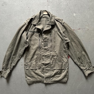 May include: Olive green military-style jacket with a collared neckline, multiple pockets, and a zip-up front. The jacket has shoulder epaulets and buttoned cuffs. The fabric appears worn, giving it a vintage aesthetic.