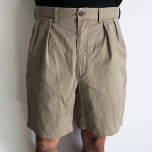 May include: Khaki-colored shorts with a pleated front and a button closure. The shorts have a belt and are made of a durable fabric. The shorts are knee-length and suitable for casual wear.