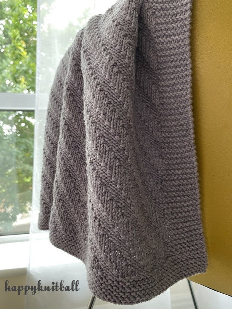 May include: A gray knitted baby blanket with a chevron pattern. The blanket is draped over a chair.