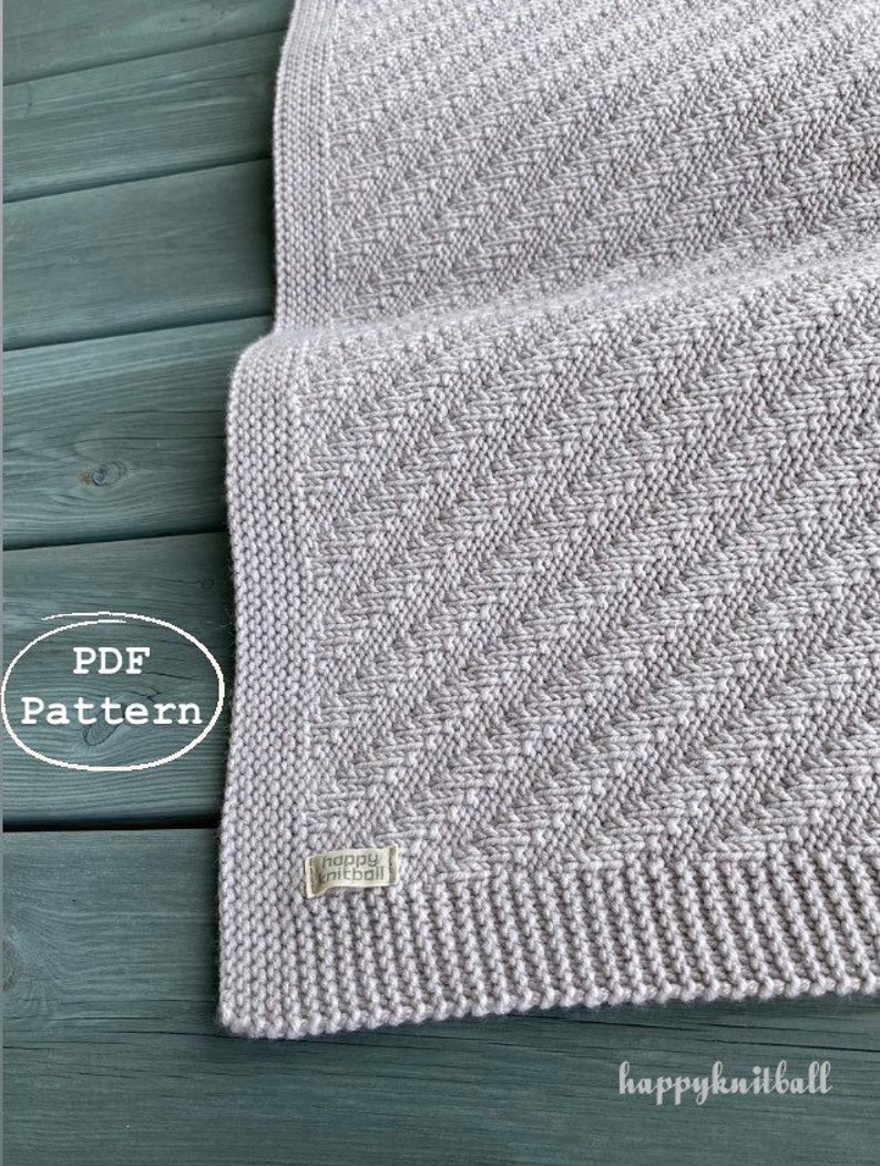 May include: A gray knitted blanket with a subtle textured pattern. The blanket is made with a soft yarn and has a finished edge. The label "happyknitball" is visible on the blanket.