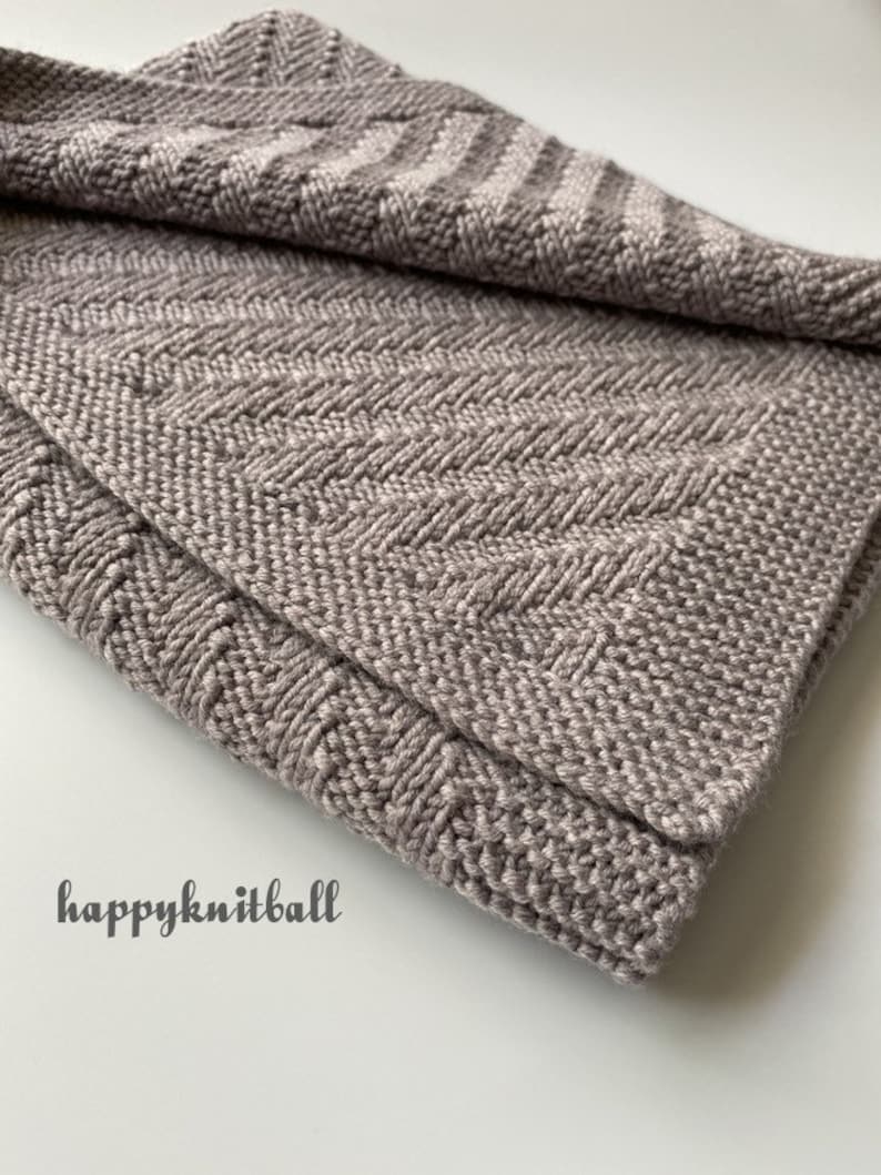 May include: A soft, gray knitted blanket with a chevron pattern. The blanket is folded in half and the edges are visible.