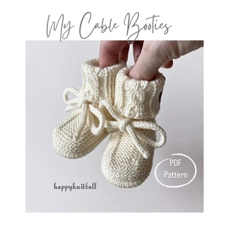 May include: A pair of cream-colored knitted booties featuring a cable knit cuff, a garter stitch foot, and a tied drawstring closure. The image includes the text My Cable Booties, happyknitball, and PDF Pattern.