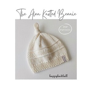 May include: An off-white knitted beanie with a top knot, featuring a ribbed brim, textured stitch patterns, and a small tag labeled happyknitball. The text reads The Alan Knotted Beanie and PDF Pattern, with the brand name happyknitball below.
