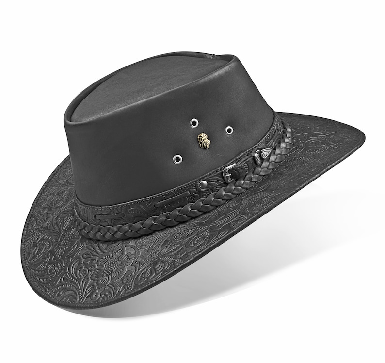 Op de afbeelding: Een zwarte leren cowboyhoed met een gevlochten band en een reli&euml;fpatroon van bloemen. De hoed heeft een kroon met een klein metalen leeuwenkopembleem en vier metalen oogjes.