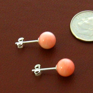 May include: A pair of pink coral stud earrings with silver posts. The earrings are about the size of a dime.