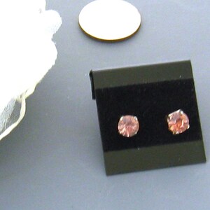 May include: A pair of small, pink stud earrings on a black velvet display card.