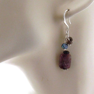 May include: Silver dangle earrings with a purple, rectangular stone, a blue stone, and brown stones.