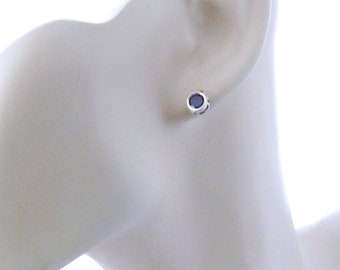 May include: A pair of silver stud earrings with a small, round, dark blue gemstone in the center.