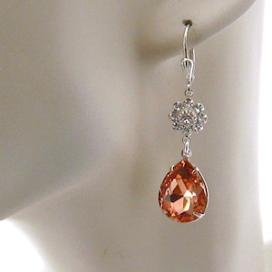 May include: A pair of silver dangle earrings with a teardrop-shaped peach-colored crystal and a smaller crystal cluster at the top.