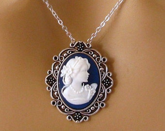 May include: Silver-toned necklace featuring an oval cameo pendant. The pendant has a dark blue background with a white profile of a woman. The cameo is framed by an ornate silver-colored border and hangs from a delicate silver chain.