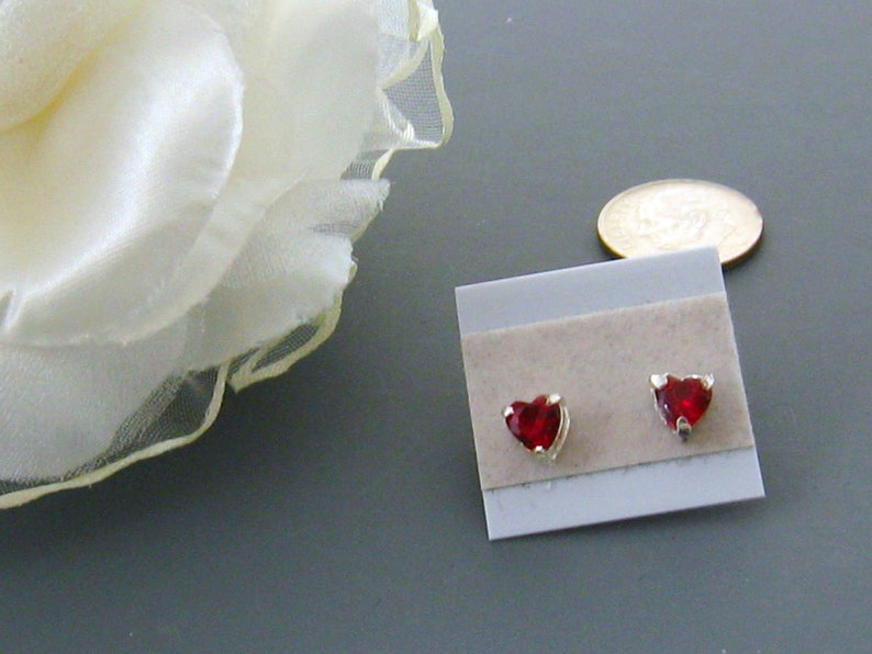 May include: A pair of heart-shaped earrings with red gemstones set in silver.