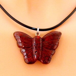 May include: A red butterfly pendant necklace with a black leather cord. The butterfly is carved from a red stone with a detailed design.