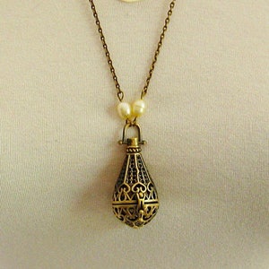 Op de afbeelding: Een gouden ketting met een delicate ketting en een hanger in de vorm van een kooi. De hanger is gemaakt van ingewikkeld metaalwerk en heeft een parel accent.