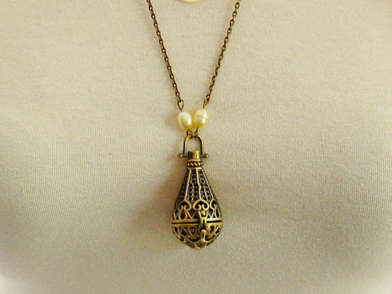 Op de afbeelding: Een gouden ketting met een delicate ketting en een hanger in de vorm van een kooi. De hanger is gemaakt van ingewikkeld metaalwerk en heeft een parel accent.