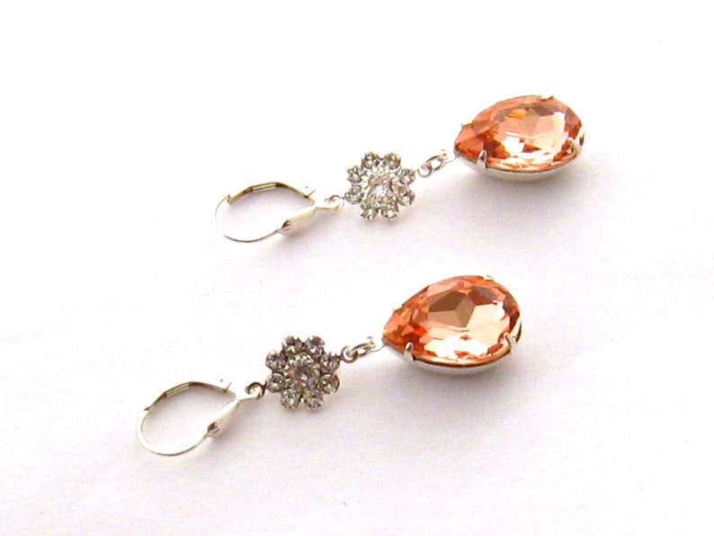 May include: A pair of peach-colored teardrop-shaped crystal earrings with silver-toned settings and a small flower-shaped crystal cluster on the top of each earring.