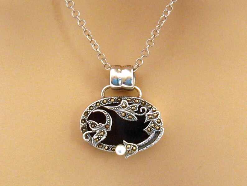 May include: A silver chain necklace with a black oval pendant featuring a floral design with a pearl accent.