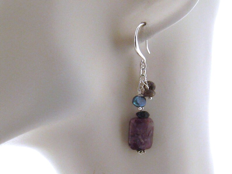 May include: Silver dangle earrings with a purple, rectangular stone, a blue stone, and brown stones.