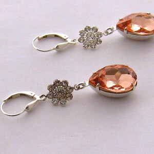 May include: A pair of silver earrings with peach-colored teardrop-shaped crystals and clear rhinestone flower accents.