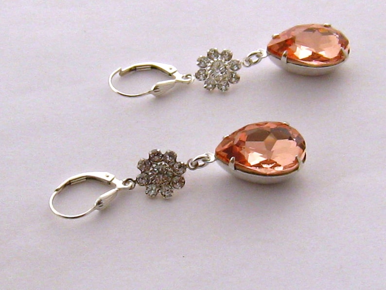 May include: A pair of silver earrings with peach-colored teardrop-shaped crystals and clear rhinestone flower accents.