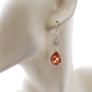May include: Silver dangle earrings with a teardrop-shaped peach-colored crystal and a smaller crystal cluster.