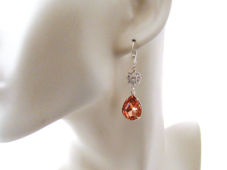 May include: Silver dangle earrings with a teardrop-shaped peach-colored crystal and a smaller crystal cluster.