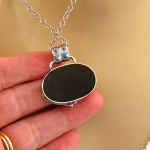 May include: A silver chain necklace with a black oval pendant. The pendant has a silver frame with blue accents.