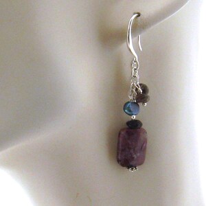 May include: Silver dangle earrings with a purple, rectangular gemstone, a dark blue bead, and a brown bead.
