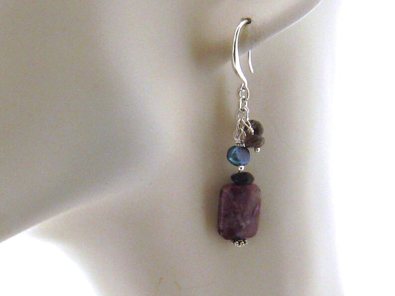 May include: Silver dangle earrings with a purple, rectangular gemstone, a dark blue bead, and a brown bead.