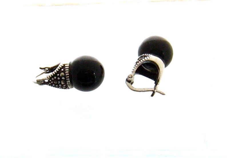 May include: A pair of black onyx earrings with silver marquise-shaped settings. The earrings have a simple, elegant design.