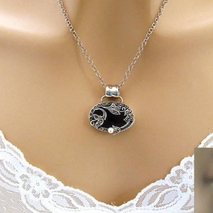 May include: A silver necklace with a black oval pendant featuring a floral design and a pearl accent. The pendant is surrounded by marcasite stones.