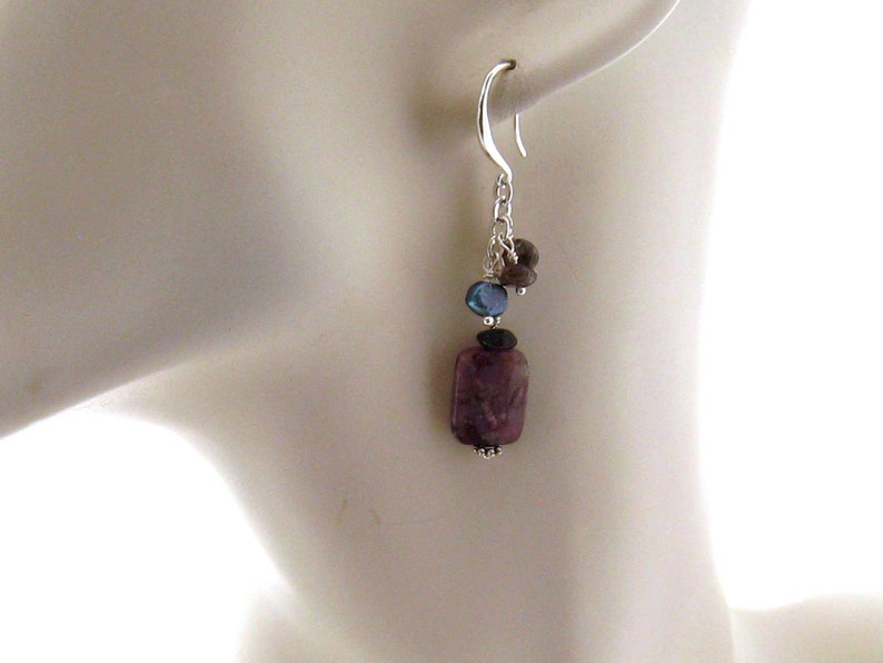 May include: Silver dangle earrings with a purple, rectangular gemstone, a blue gemstone, and a brown gemstone.