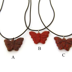 May include: Three red butterfly necklaces with black cords. The butterflies are carved from red jasper and have a detailed design. The necklaces are labeled A, B, and C.